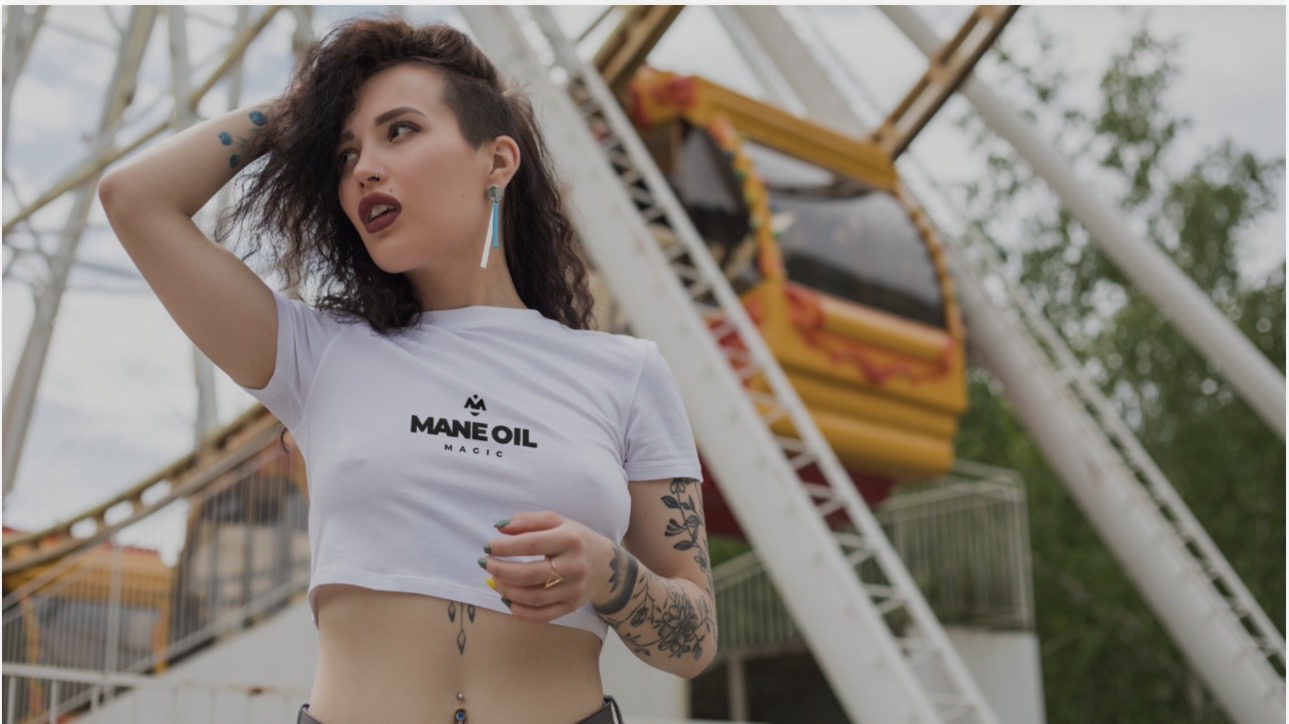 Woman wearing a white Mane Oil Magic crop tee at a fairground
